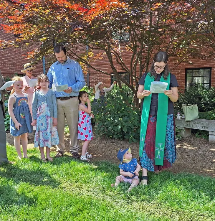 Outdoor worship with families beneath a leafy tree